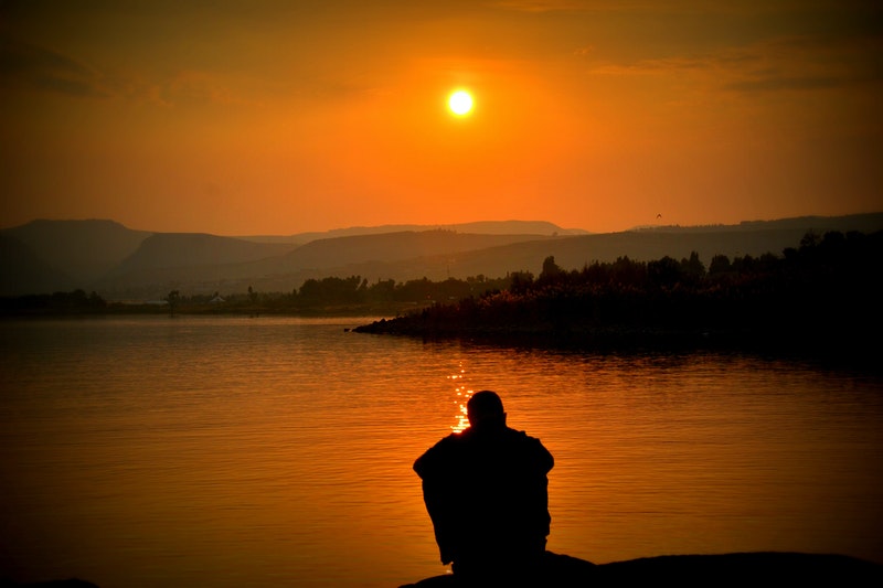 Image of a man sitting by the ocean at sunset