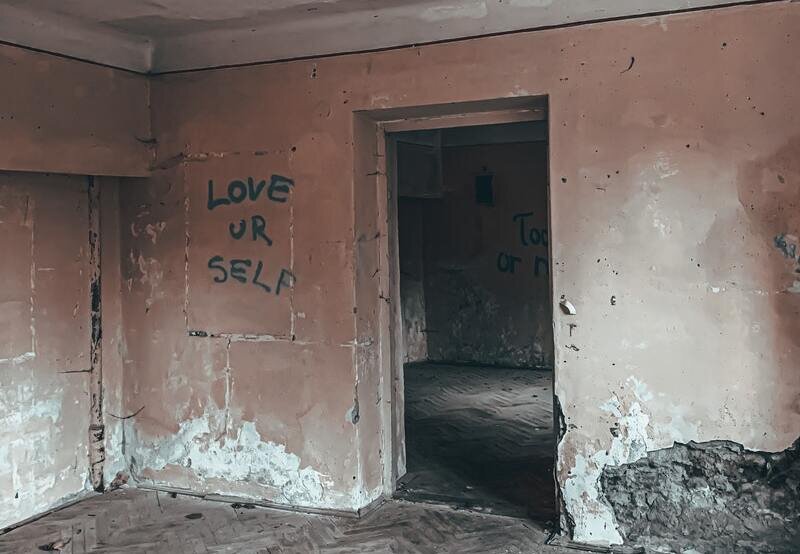 Image of an abandoned house will a wall that says "love yourself"