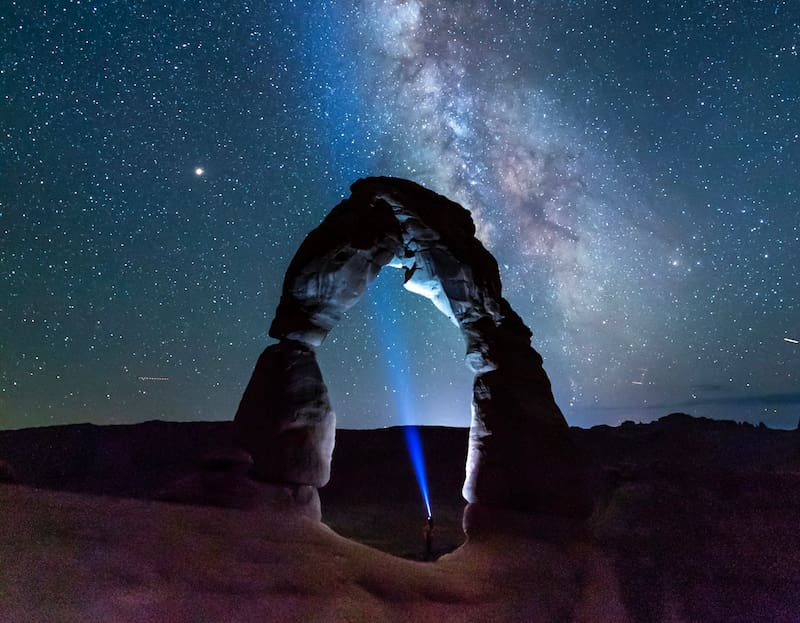Image of a person shining their torch into the sky under a pillar of rock symbolic of soul work
