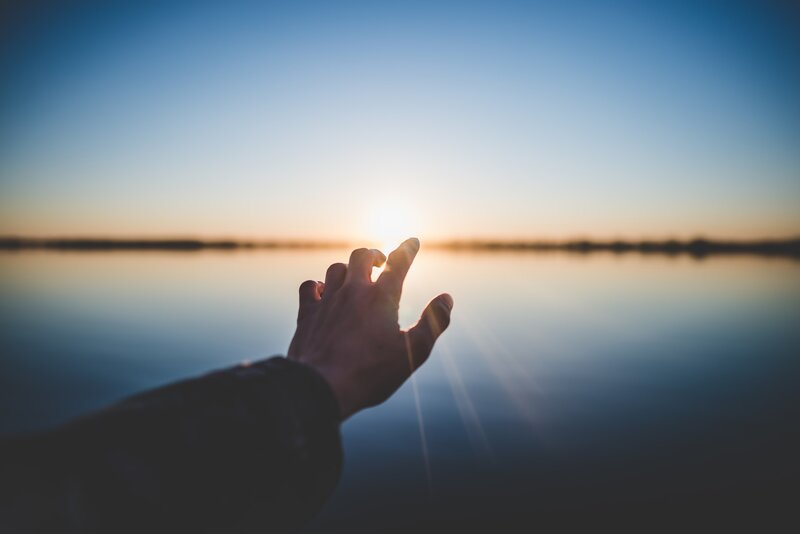 Image of a hand reaching toward the light in the horizon