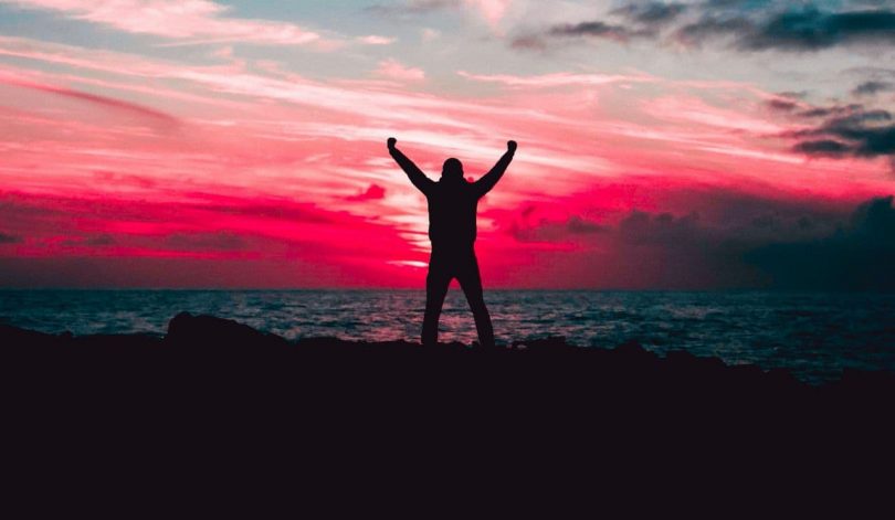 Image of a happy person near the ocean at sunset bursting with inner strength