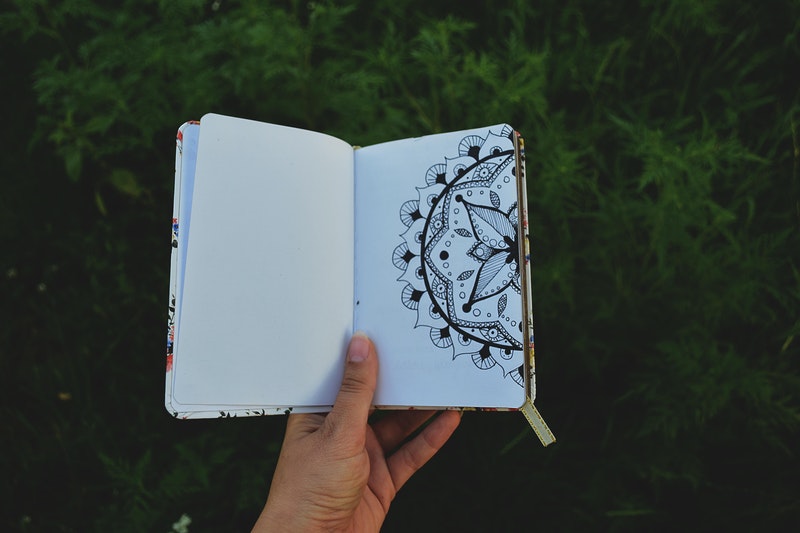 Image of a woman holding up her journal next to a green backdrop