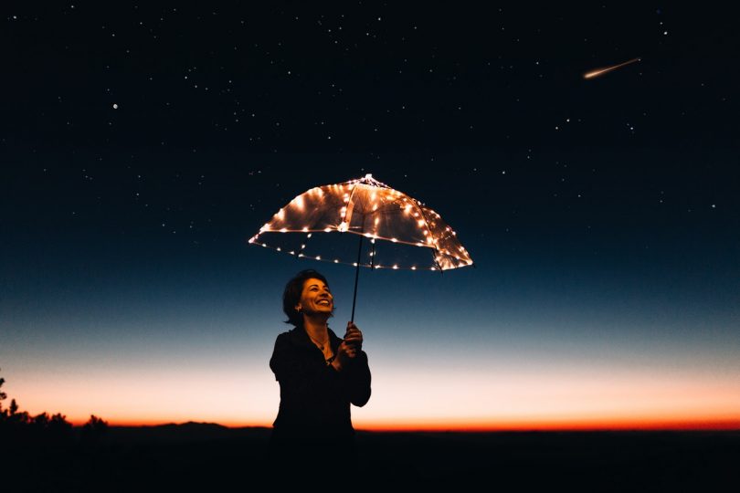 Image of a woman holding an umbrella smiling learning how to be true to herself