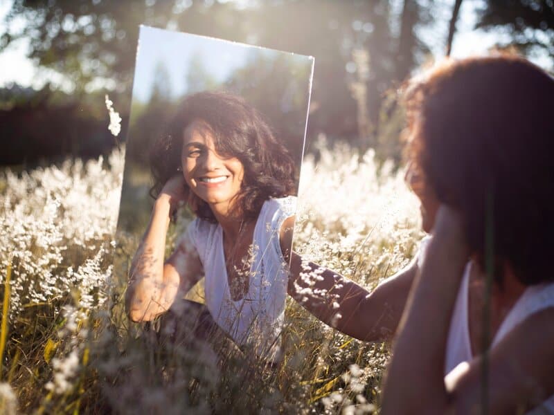 Image of a woman smiling into a mirror practicing mirror work