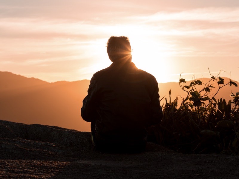 Image of a man sitting in front of the sunset