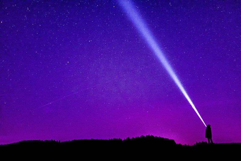 Image of a person with a flashlight against a purple sky