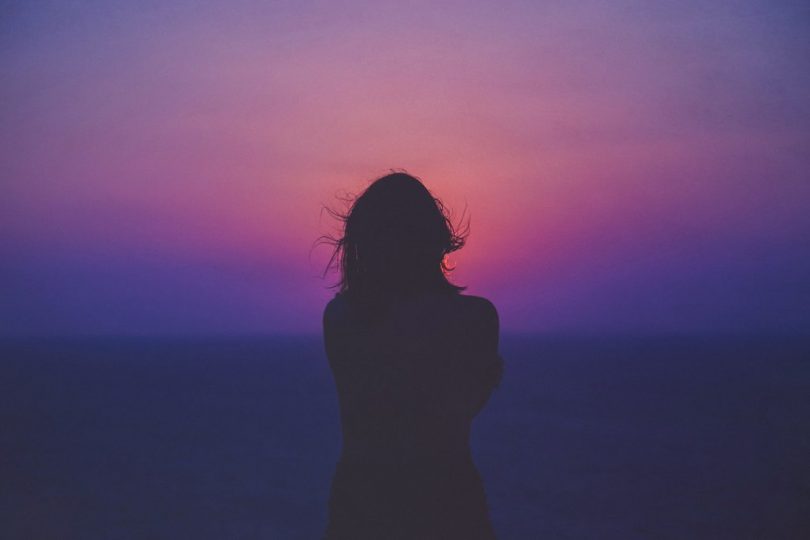 Image of a solitary woman in front of a sunset trying to learn how to deal with loneliness