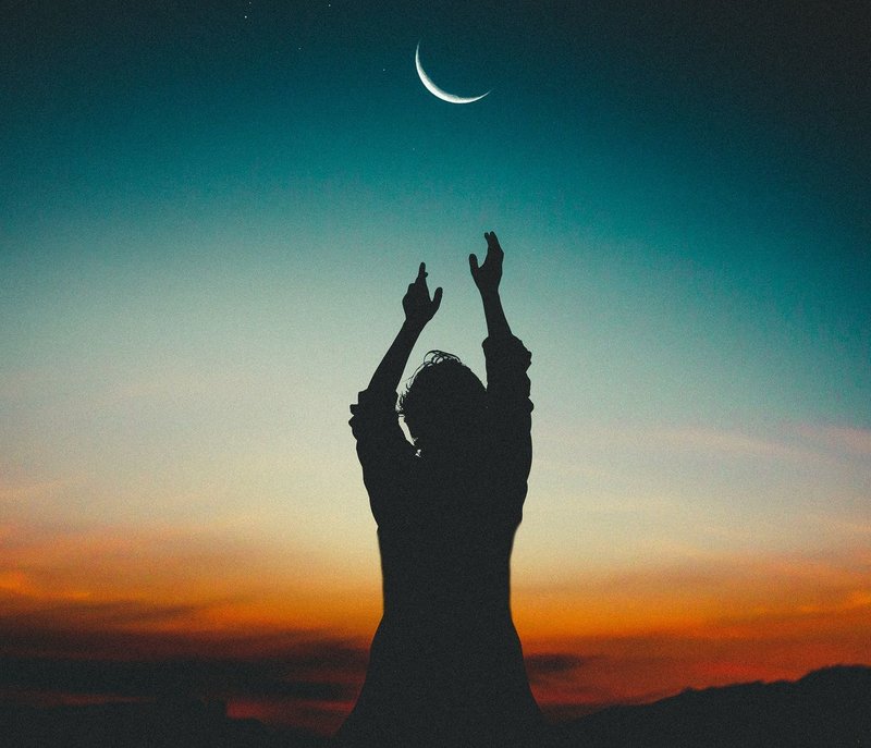 Image of a person reaching for the moon at sunset