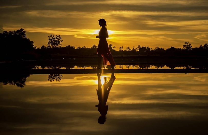 Image of a woman walking along the river at sunset