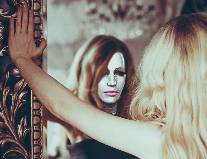 Image of a woman wearing a mask looking at herself in the mirror