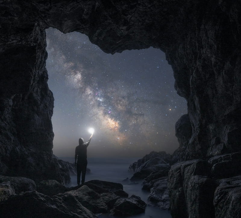 Image of a rock doorway leading to the cosmos with a person standing shining a light symbolic of ensoulment