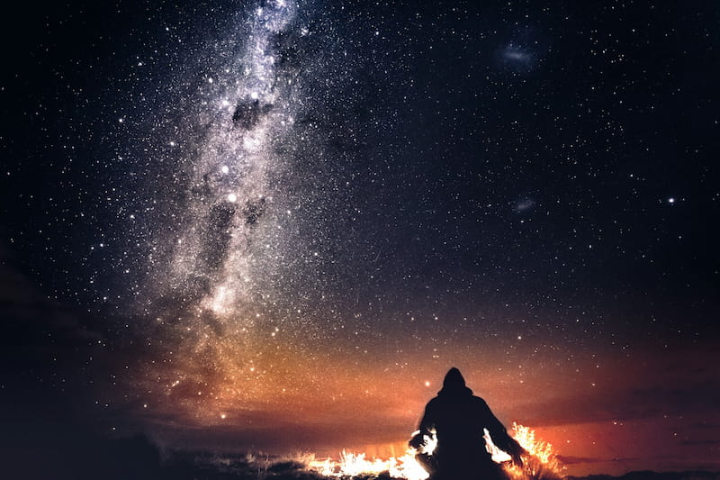 Image of a man sitting with the fire beneath the stars