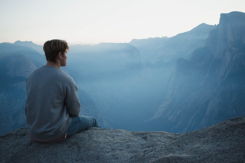 Image of a man practicing spiritual meditation overlooking some blue mountains