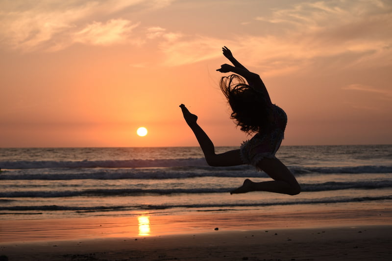 Image of a woman jumping for joy at sunset in front of the beach