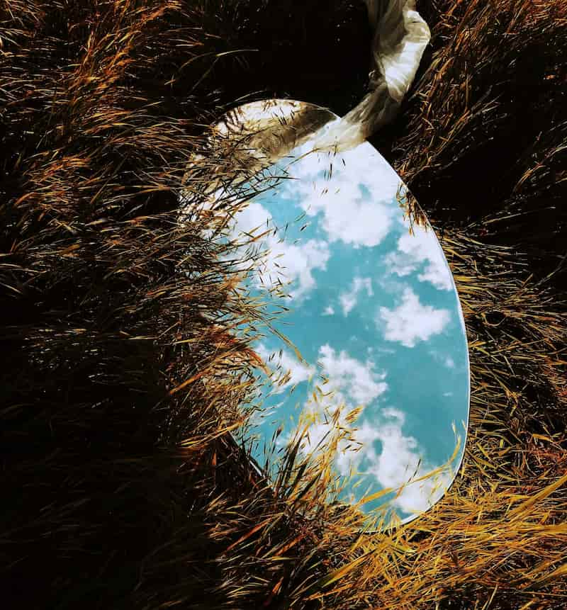 Image of a mirror reflecting the sky above in a paddock of grass