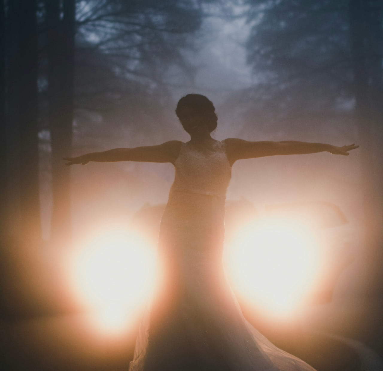 Image of a woman symbolizing the soul standing in front of some high beam headlights in a dark forest symbolizing feeling stuck on the soul's path