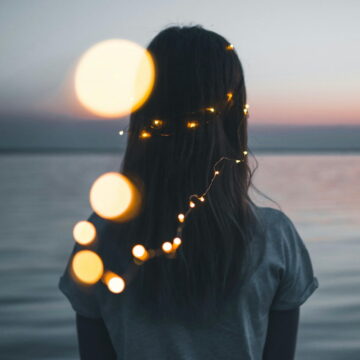 Image of a lone wolf empath woman staring across a lake with fairy lights