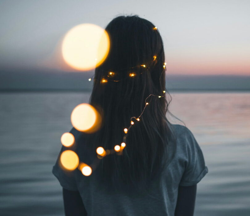 Image of a lone wolf empath woman staring across a lake with fairy lights
