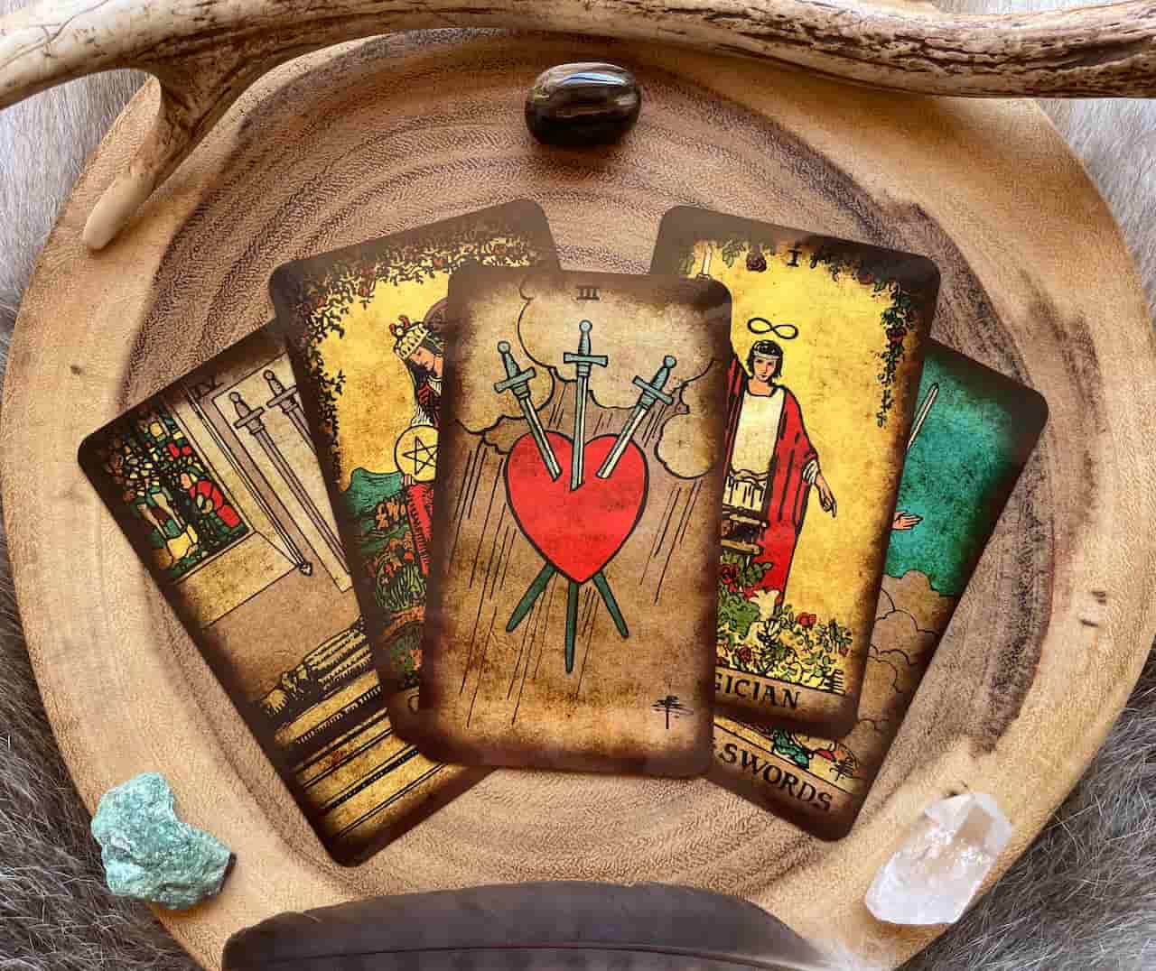 Image of five tarot cards on a wooden board surrounded with feathers and stones used to help someone deal with existential panic, dread, and anxiety