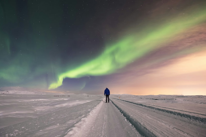 Image of a man in the snow standing under the aurora borealis