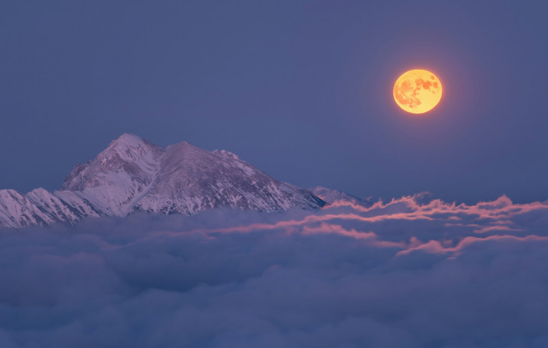 Image of a full snow moon over an icy mountain peak