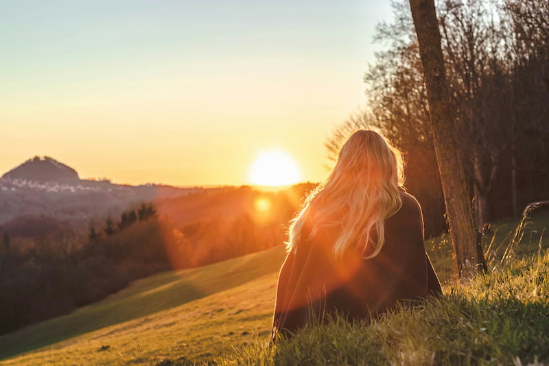 Image of a relaxed woman sitting on a hill watching the sunset
