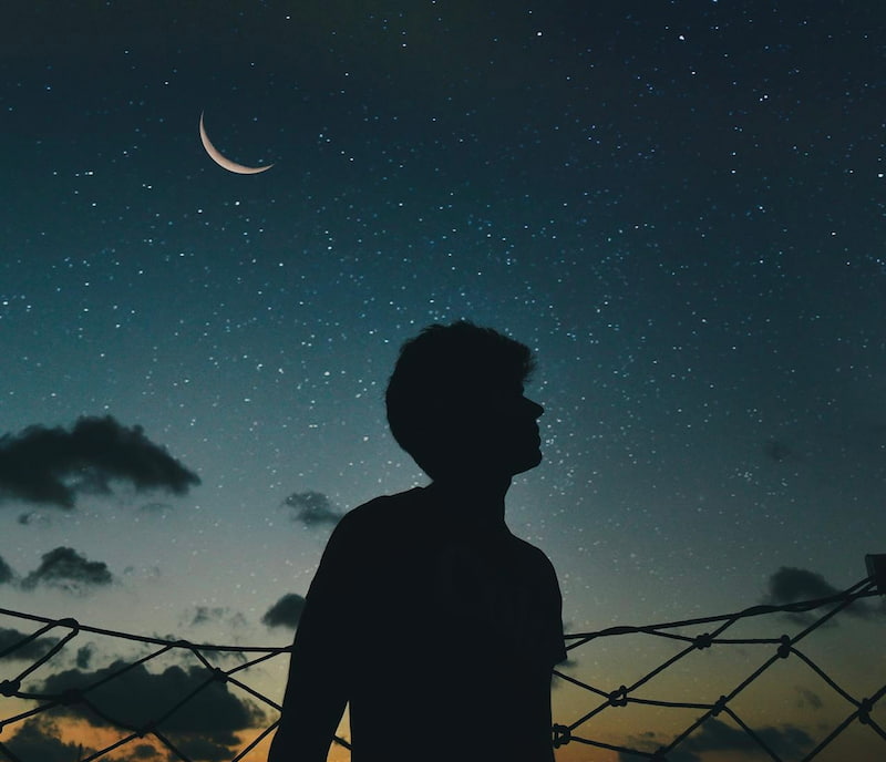 Image of a man standing underneath a crescent moon at night