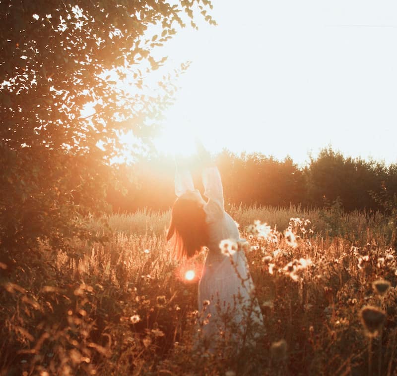 Image of a joyful woman beneath the morning sun in a field of flowers symbolizing soul recovery