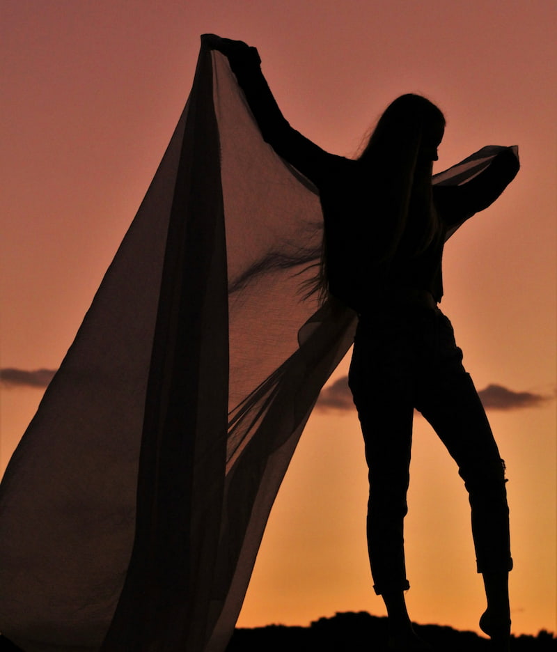 Image of a woman at sunset holding up a shawl symbolizing freedom