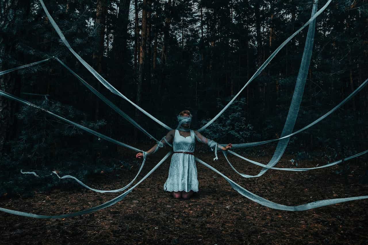 image of a woman in a dark forest with bandages tied to her and the trees symbolic of the types of people pleasing and giving away energy